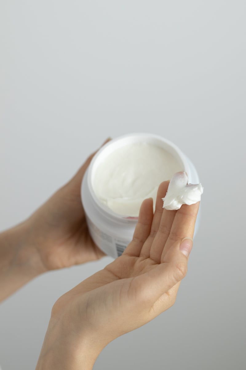 Person Holding White Cream in White Plastic Container